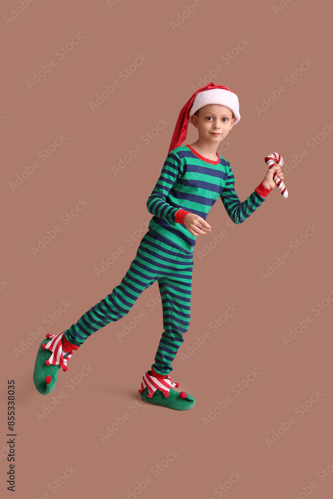 Cute little boy in Christmas pajamas with candy cane toy on brown background Cute little boy in Christmas pajamas with candy cane toy on brown background