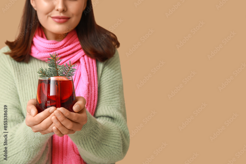 Young woman in scarf with glass of hot mulled wine on brown background Young woman in scarf with glass of hot mulled wine on brown background