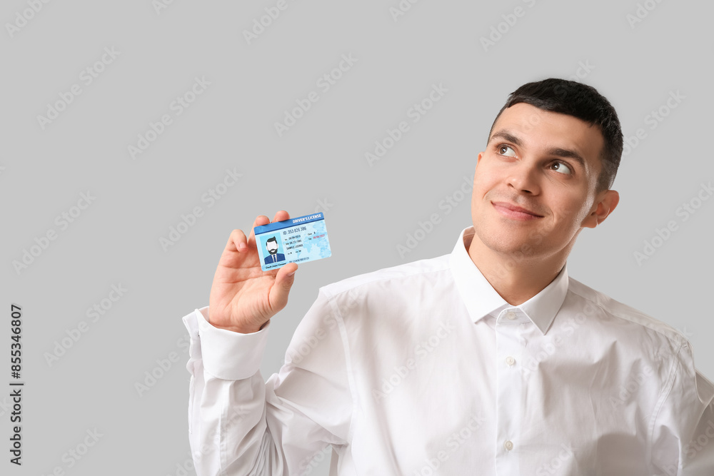 Young happy man with driver license on grey background Young happy man with driver license on grey background