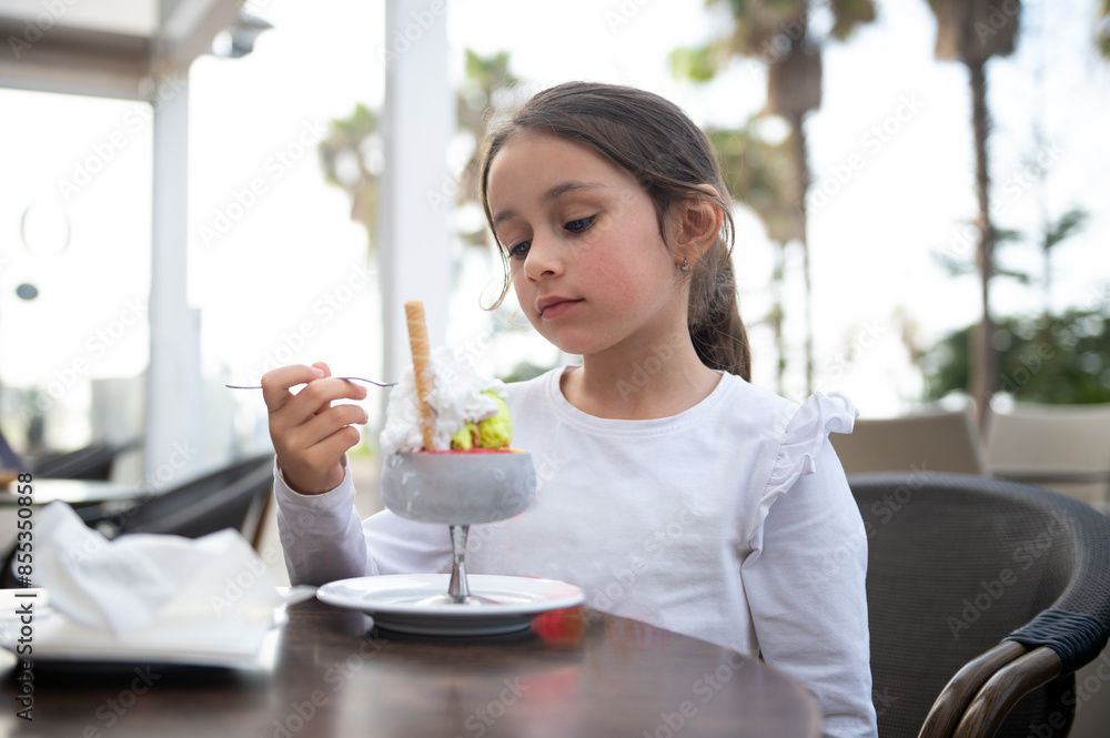Little girl enjoying ice cream sundae in outdoor cafe Little girl enjoying ice cream sundae in outdoor cafe