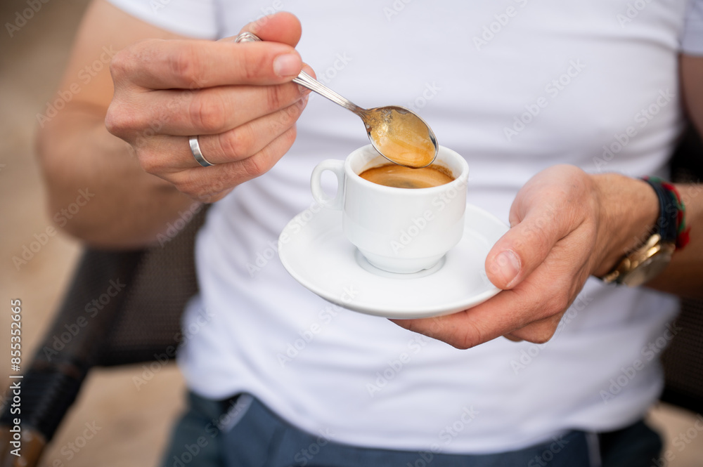 Man stirring a cup of espresso with spoon in hand Man stirring a cup of espresso with spoon in hand