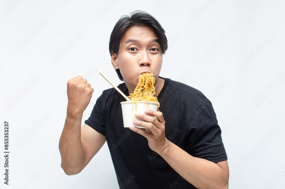 young Asian man enjoys his noodles with deep pleasure using chopstick and paper bowl. man in black tshirt eats noodles with great enthusiasm. young Asian man enjoys his noodles with deep pleasure using chopstick and paper bowl. man in black tshirt eats noodles with great enthusiasm.