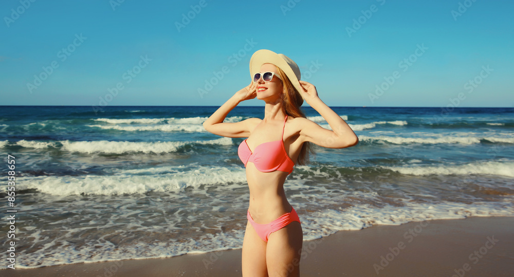 Naklejka premium Summer vacation, beautiful happy slim woman in pink bikini swimsuit, tourist hat on the beach on sea