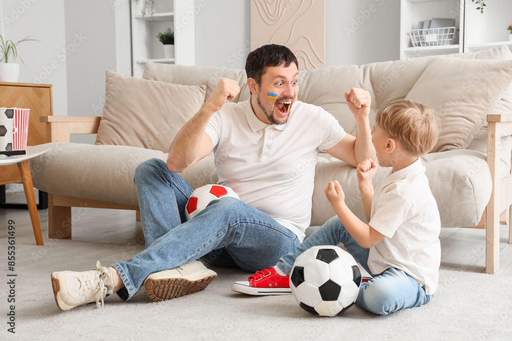 Young father and little son with soccer balls sitting on floor at home Young father and little son with soccer balls sitting on floor at home