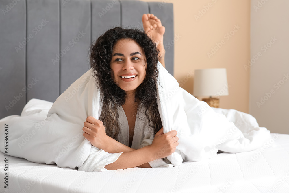 Young African-American woman with blanket lying on soft mattress at home Young African-American woman with blanket lying on soft mattress at home