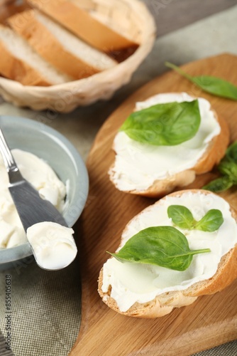 Delicious sandwiches with cream cheese and basil leaves on wooden table, closeup