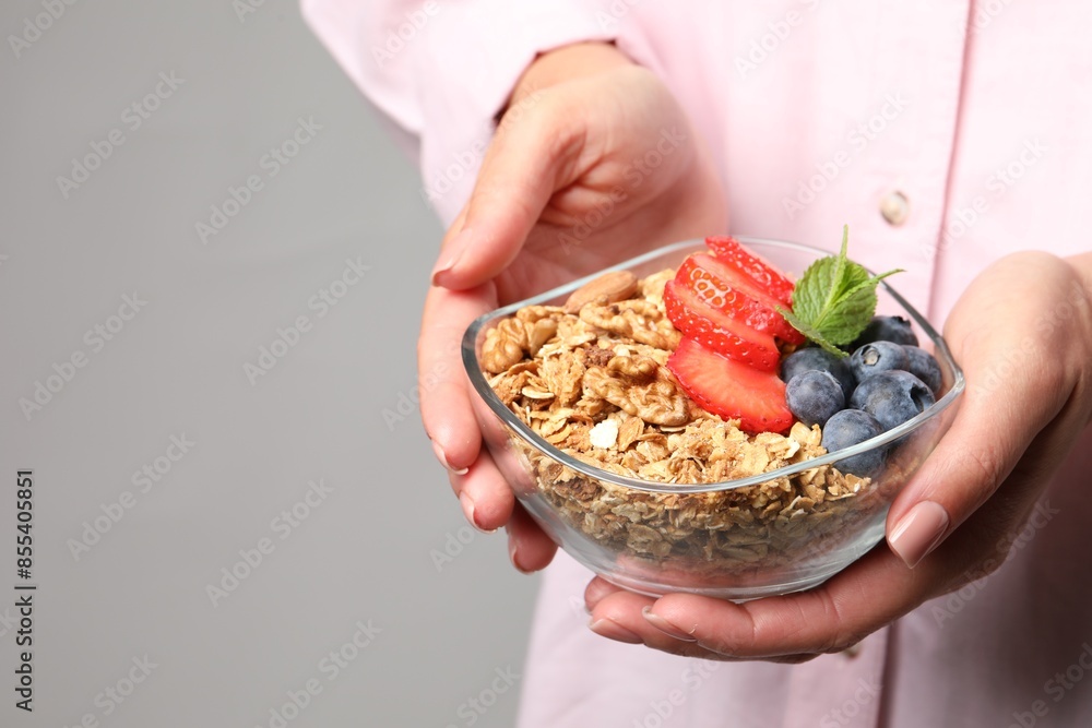 Woman holding bowl of tasty granola with berries, nuts and mint on light grey background, closeup. Space for text Woman holding bowl of tasty granola with berries, nuts and mint on light grey background, closeup. Space for text