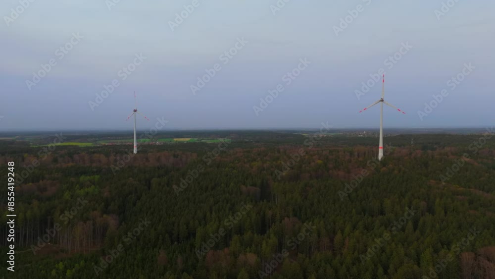 Aerial view of wind farm turbines set up in countryside with forest. Producing power using energy of nature. Incorporating technology into environment of nature. Cloudy sky. Electricity production. Aerial view of wind farm turbines set up in countryside with forest. Producing power using energy of nature. Incorporating technology into environment of nature. Cloudy sky. Electricity production.