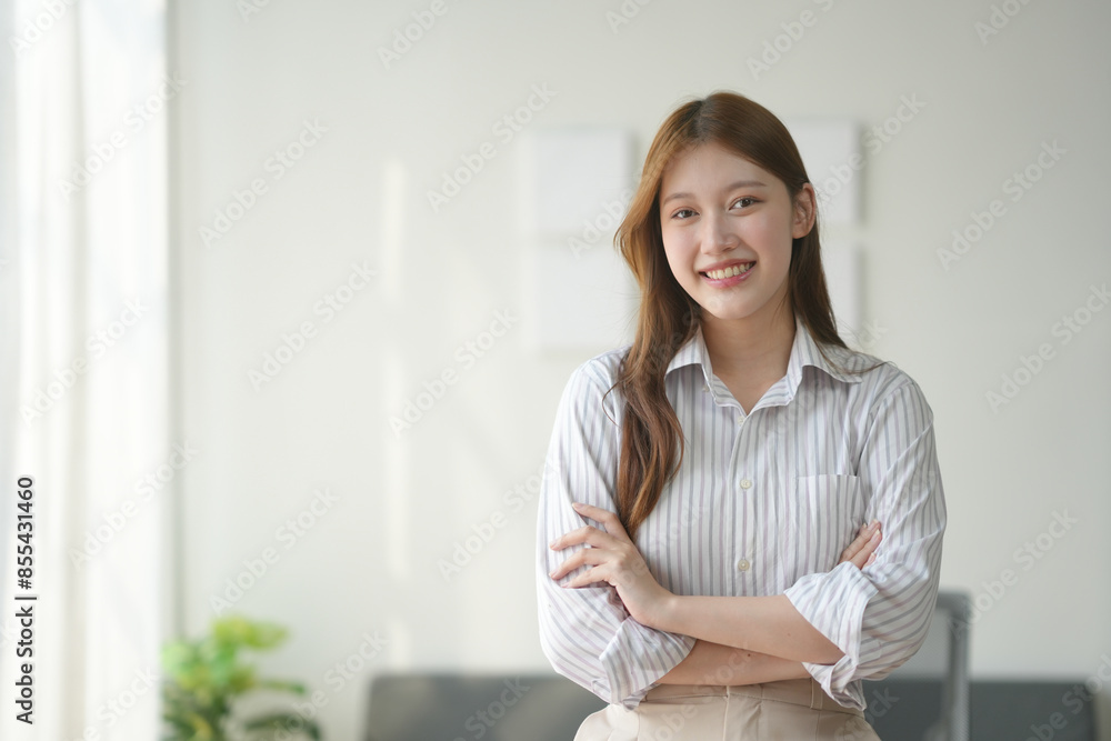 Confident woman with crossed arms, standing in bright room, wearing striped shirt, smiling at camera. Professional, business, indoor portrait. Confident woman with crossed arms, standing in bright room, wearing striped shirt, smiling at camera. Professional, business, indoor portrait.