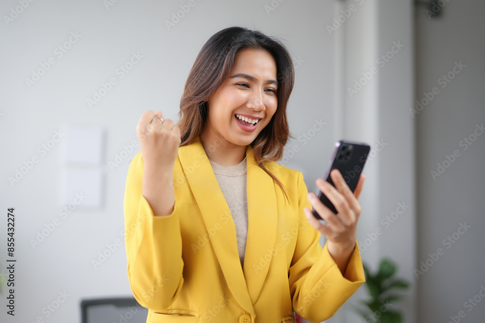 Excited woman in a yellow blazer celebrating good news on her smartphone in a modern office setting, showing joy and success. Excited woman in a yellow blazer celebrating good news on her smartphone in a modern office setting, showing joy and success.