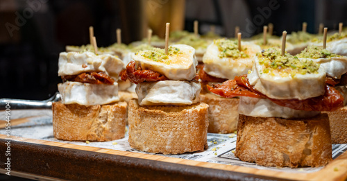 Typical snack of Basque Country, pinchos or pinxtos skewers with small pieces of bread, sundried tomatoes, goat cheese served in bar in San-Sebastian or Bilbao, Spain, close up
