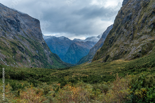 Lush green valley under huge rugged mountain peaks and tall cliffs