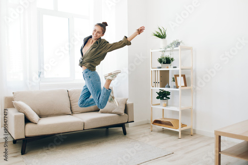 Joyful Woman Jumping in a Playful Indoor Apartment, Relaxing on Sofa with Music and Carefree Smile