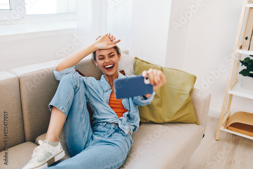 Joyful Woman Relaxing on Cozy Sofa, Holding Smartphone and Smiling