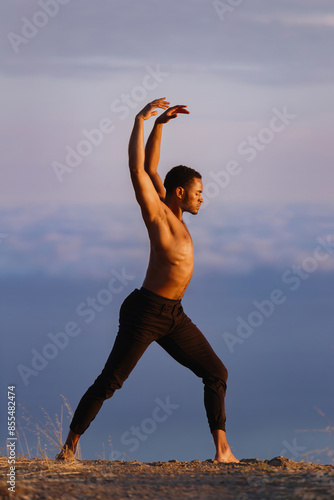 Elegant male ballet dancer doing a majestic pose on a grassy ridge at sunset. Behind him are heavenly clouds. photo