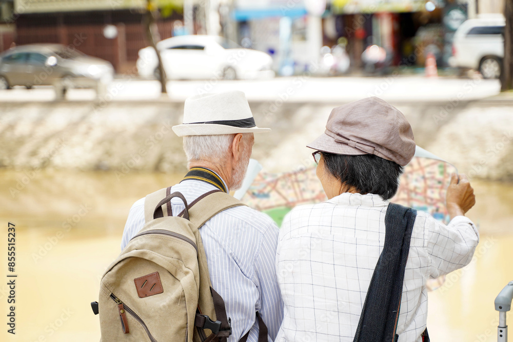Closeup back view of American senior tourist man with his tour guide are looking at city maps to find tourist attractions on blurred of city background. Senior tourist concept Closeup back view of American senior tourist man with his tour guide are looking at city maps to find tourist attractions on blurred of city background. Senior tourist concept