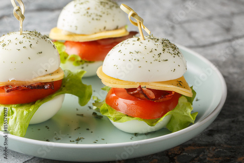 Snack on skewers of hard-boiled eggs with cheese, bacon, tomato and lettuce close-up in a plate on the table. Horizontal