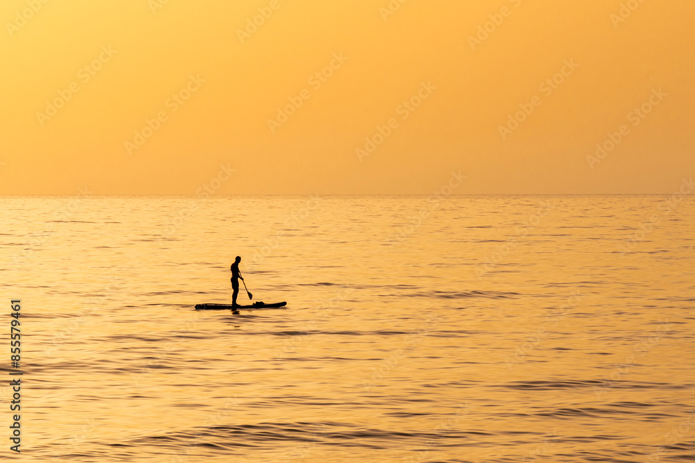 Fototapeta premium A man on his paddleboard in silhouette out in the Mediterranean Sea near Haifa, Israel during the golden hour with a beautiful orange sunset. 