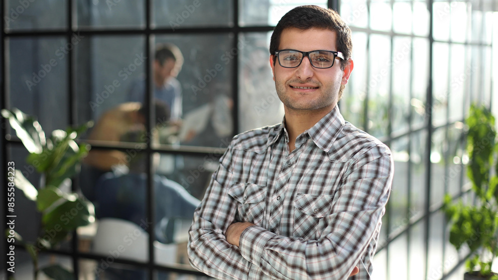 Young businessman with arms crossed standing in office lobby