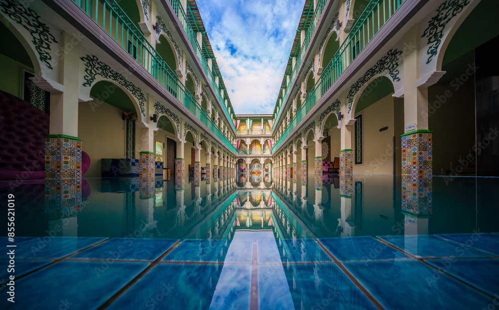 Fototapeta premium Beautiful courtyard featuring arched walkways and a reflective pool, showcasing intricate architectural details and colorful tiles.