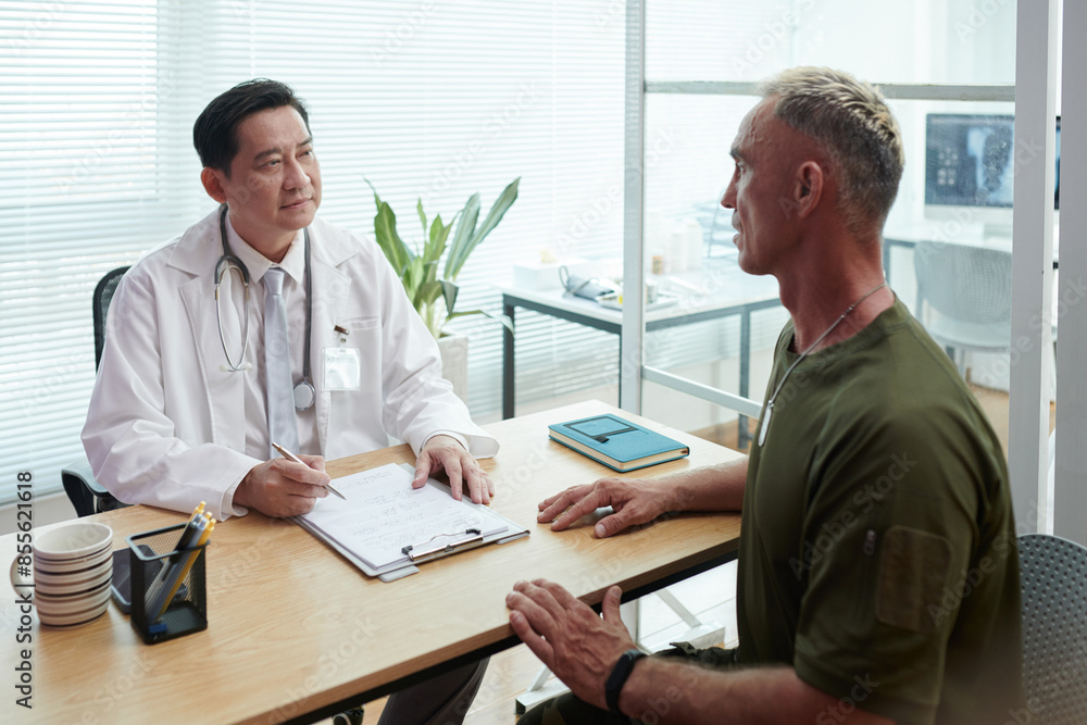 Doctor prescribing treatment for soldier during his appointment at hospital Doctor prescribing treatment for soldier during his appointment at hospital