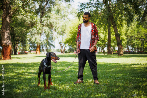 African american man standing with doberman dog on lawn in park