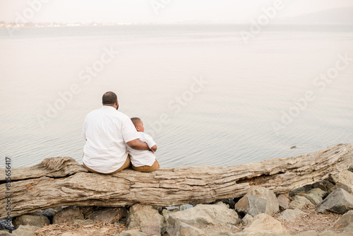 Father and son sitting on a log looking out at the water photo