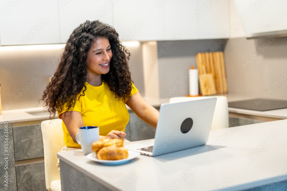 Woman attending a video call with laptop while eating breakfast Woman attending a video call with laptop while eating breakfast