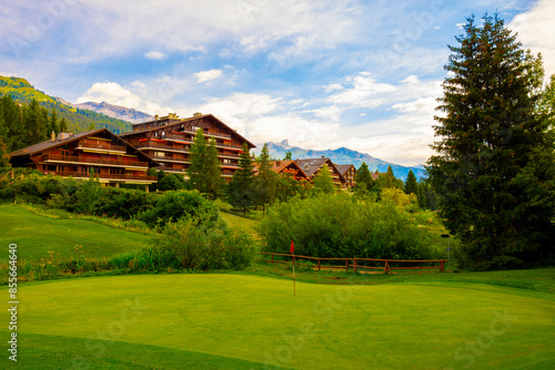 Village with House and Hotel with Panoramic View over Mountain with Clouds and Golf Course in a Sunny Summer Day in Crans Montana, Valais, Switzerland.