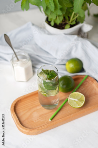 Mojito cocktail with limes, drinking straw, mint leaves in pot, sugar on white table, lifestyle home kitchen table, homemade summer fresh drink ingredients