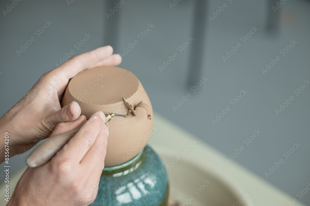 Fototapeta premium A potter works with a tool on a potter's wheel. Close-up of a man's hands. 