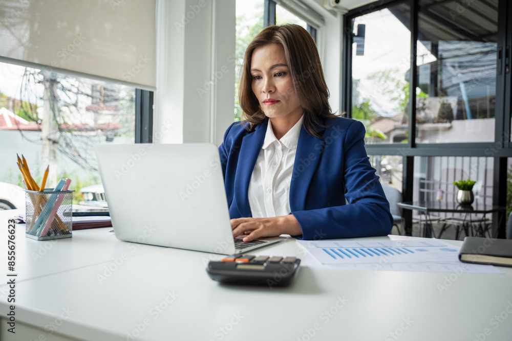 Businesswoman sitting at desk on couch in workplace or at home working on laptop and analyzing data on charts and graphs and writing on papers to make business plan and strategies for company, startup Businesswoman sitting at desk on couch in workplace or at home working on laptop and analyzing data on charts and graphs and writing on papers to make business plan and strategies for company, startup