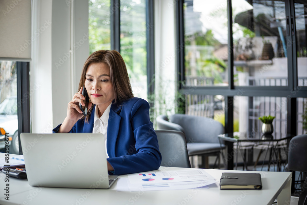 Businesswoman sitting at desk on couch in workplace or at home working on laptop and analyzing data on charts and graphs and writing on papers to make business plan and strategies for company, startup Businesswoman sitting at desk on couch in workplace or at home working on laptop and analyzing data on charts and graphs and writing on papers to make business plan and strategies for company, startup