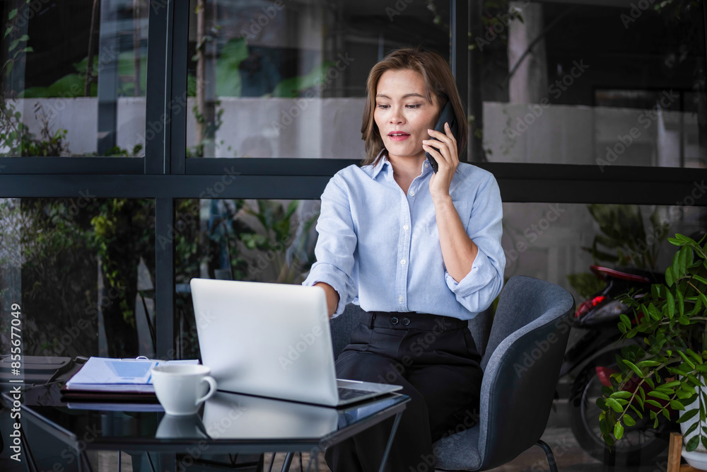 Businesswoman sitting at desk on couch in workplace or at home working on laptop and analyzing data on charts and graphs and writing on papers to make business plan and strategies for company, startup Businesswoman sitting at desk on couch in workplace or at home working on laptop and analyzing data on charts and graphs and writing on papers to make business plan and strategies for company, startup