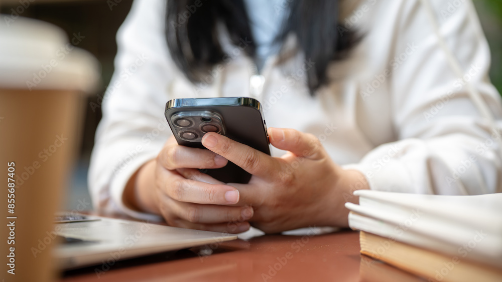 A cropped image of a woman using her smartphone at a table in a cafe, working remotely. A cropped image of a woman using her smartphone at a table in a cafe, working remotely.