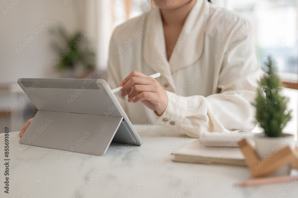 A woman holding a stylus pen and using her digital tablet, working remotely from a cafe. A woman holding a stylus pen and using her digital tablet, working remotely from a cafe.
