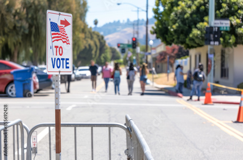 To Vote sign with American flag, city street, people in background, election day, community participation. © PixelGallery
