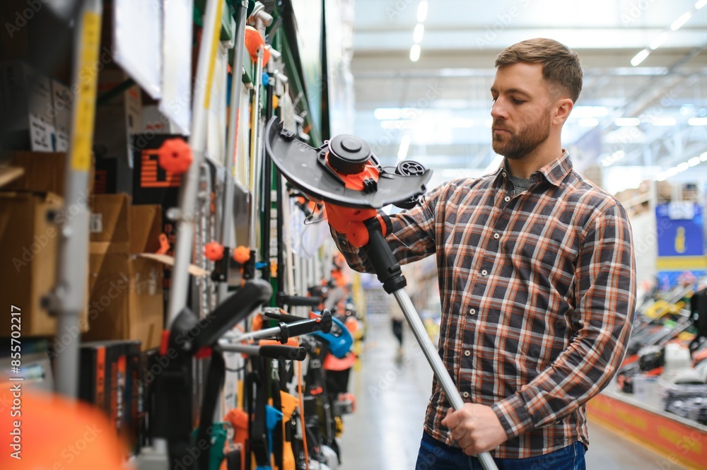 a young man in a gardening equipment store chooses an electric trimmer for mowing lawn grass a young man in a gardening equipment store chooses an electric trimmer for mowing lawn grass