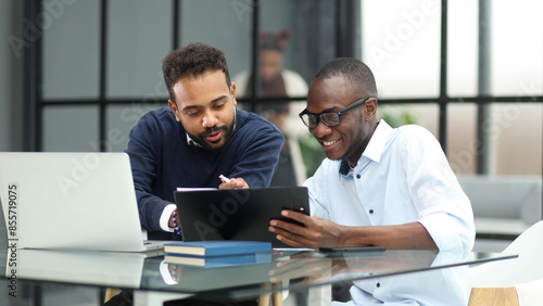 colleagues sitting together at a table in a modern office talking and using a laptop