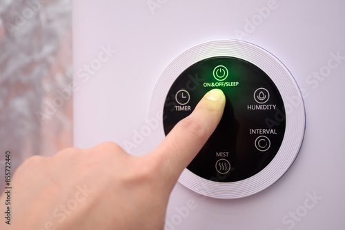 Close up of hand pressing on the digital on and off button of a smart humidifier in a smart home or green house.
