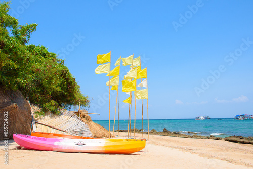 Colorful kayaks on the beach decorated with a summer holiday theme and yellow flags on the island of Koh Larn. Beautiful tropical beach and sea views and water activity equipment.
