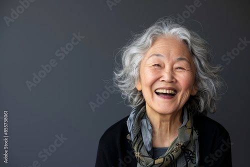 Portrait of a content asian woman in her 70s laughing isolated in minimalist or empty room background © CogniLens