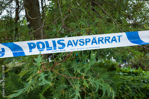 A Swedish police barricade tape blue and white on background of a green trees