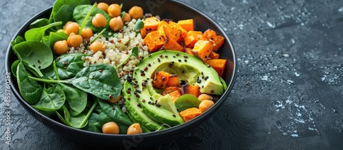 Avocado, quinoa, roasted sweet potato, spinach and chickpeas salad in black bowl. Top view, copy space