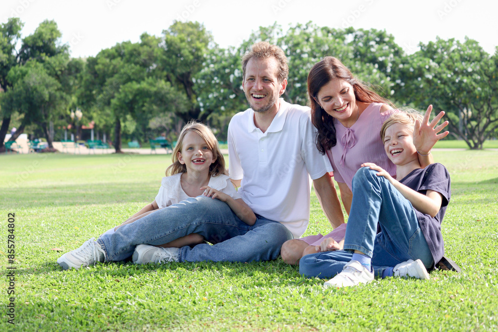 Happy family sitting on green grass at the park, smiling father, mother, son and daughter spending time together outdoors in beautiful garden on weekend holiday. Parents and kids have fun outside. Happy family sitting on green grass at the park, smiling father, mother, son and daughter spending time together outdoors in beautiful garden on weekend holiday. Parents and kids have fun outside.