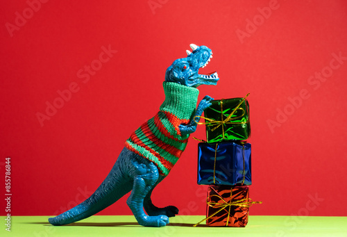 Happy blue dinosaur in knitted sweater with stack of gifts on red green background