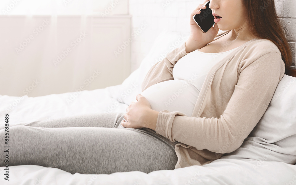 Cropped of pregnant woman is sitting on a bed, engaged in a phone conversation. She appears relaxed and focused as she communicates over the cell phone. Cropped of pregnant woman is sitting on a bed, engaged in a phone conversation. She appears relaxed and focused as she communicates over the cell phone.