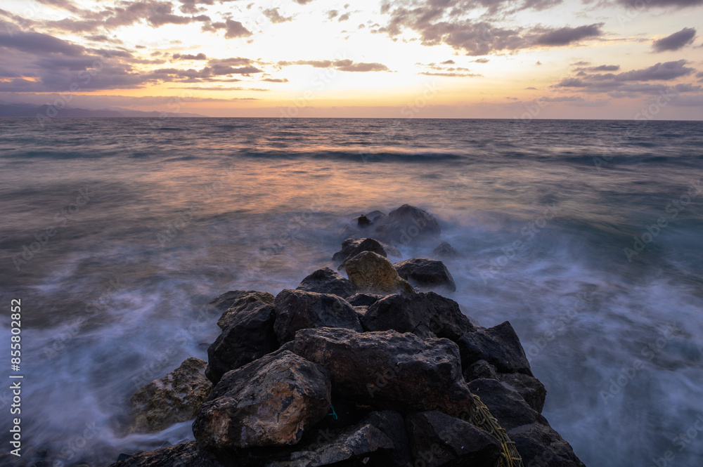 Dramatic sunset over the Mediterranean Sea with rocks in the foreground. Cloudy sky and waves on the beach. 1 Dramatic sunset over the Mediterranean Sea with rocks in the foreground. Cloudy sky and waves on the beach. 1
