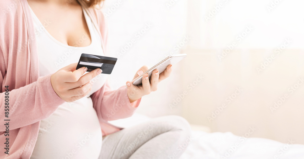 Preparing for maternity. Pregnant woman buying baby goods online with credit card and cellphone, panorama with free space Preparing for maternity. Pregnant woman buying baby goods online with credit card and cellphone, panorama with free space