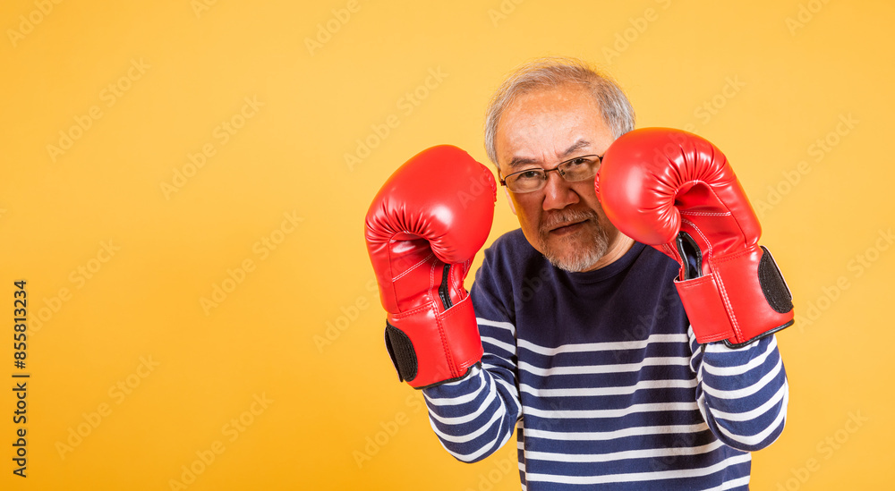 Portrait Asian old man wearing glasses wear two red boxing gloves studio shot isolated yellow background, smiling happy elderly man gray haired healthy fighter lifestyle concept Portrait Asian old man wearing glasses wear two red boxing gloves studio shot isolated yellow background, smiling happy elderly man gray haired healthy fighter lifestyle concept